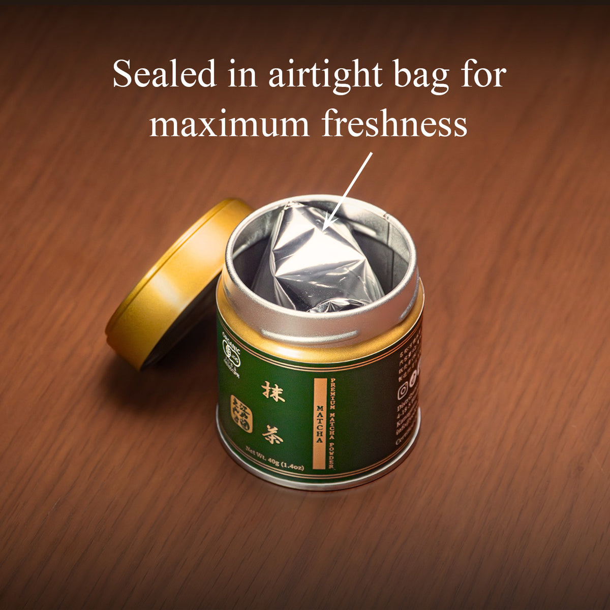 Open Premium Matcha tin on a wooden surface with the gold lid beside it, revealing the inner foil bag, text 'Sealed in airtight bag for maximum freshness'.