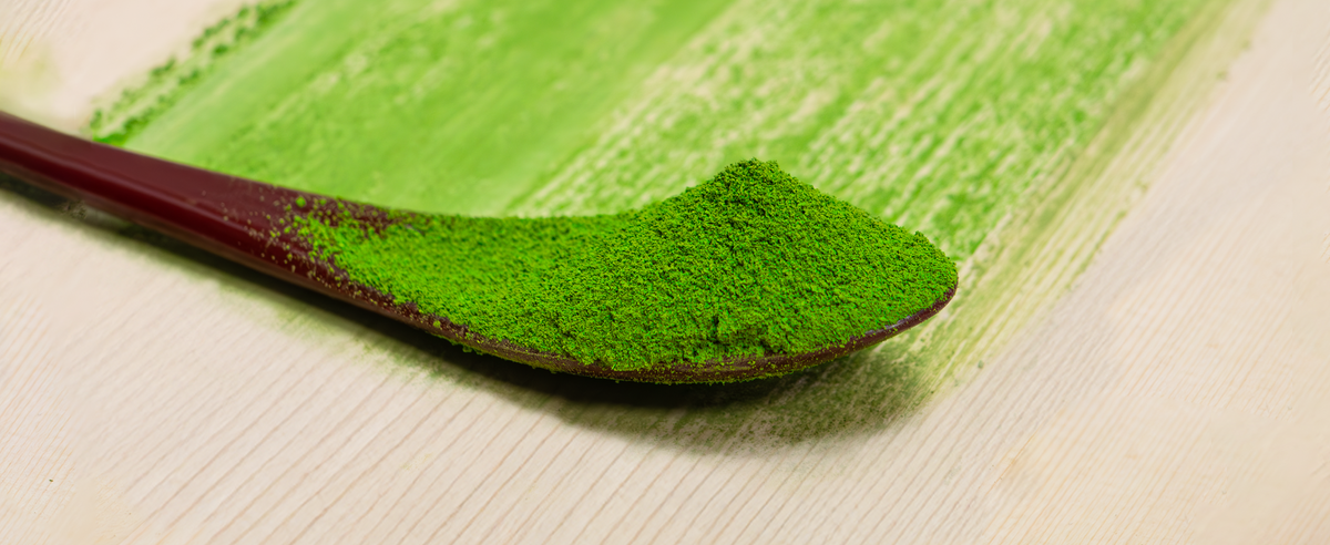 Spoonful of green matcha powder on a wooden surface