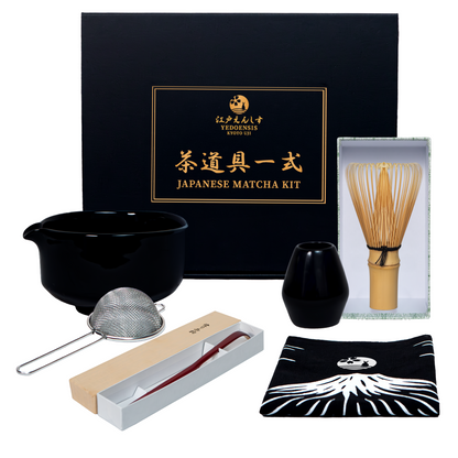 A Japanese matcha tea kit arranged on a white background with its black presentation box. The set includes a black ceramic whisk bowl, metal strainer, bamboo whisk, a chasentate whisk stand, bamboo scoop, and folded originally designed Japanese cloth.