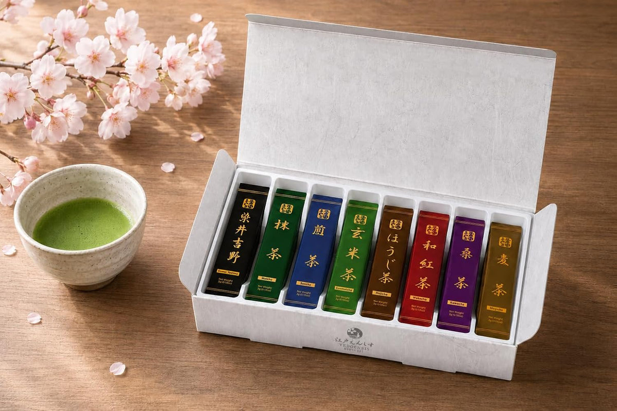 Opened white sampler box on a wooden table showing the eight tea sticks upright in their tray, beside a bowl of whisked matcha and cherry blossom branches.