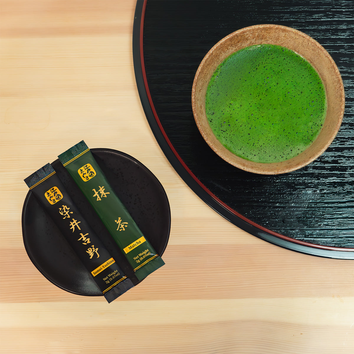 Overhead view of Somei-Yoshino and Matcha sticks on a black plate next to a bowl of bright green whisked matcha on a lacquer tray.