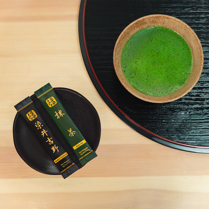 Overhead view of Somei-Yoshino and Matcha sticks on a black plate next to a bowl of bright green whisked matcha on a lacquer tray.