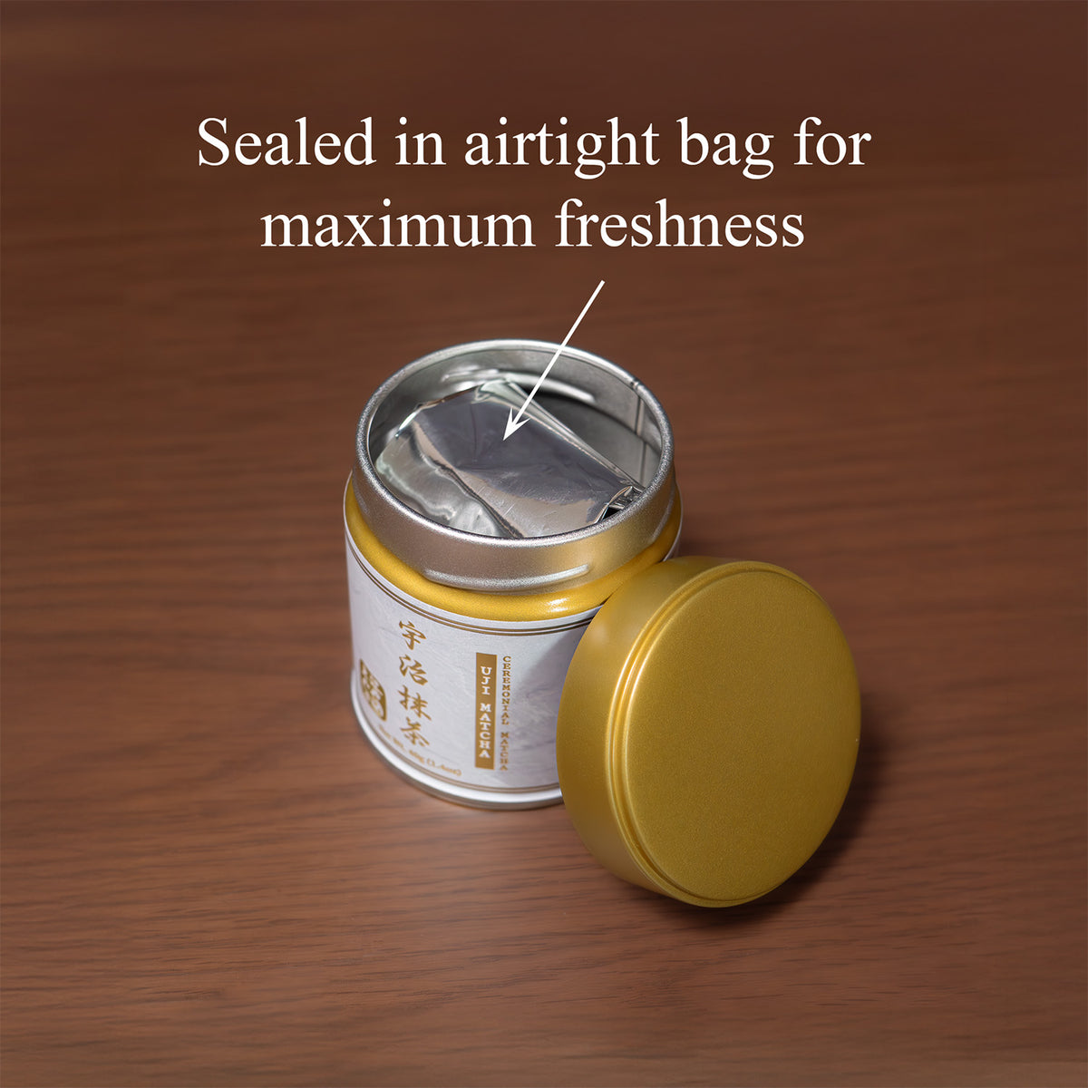 Open Uji Ceremonial Matcha tin on a wooden surface with the gold lid beside it, revealing the inner foil bag, text 'Sealed in airtight bag for maximum freshness'.